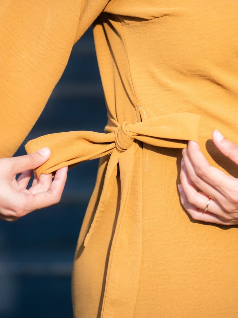 Hands tying a soft fabric bow on a mustard garment